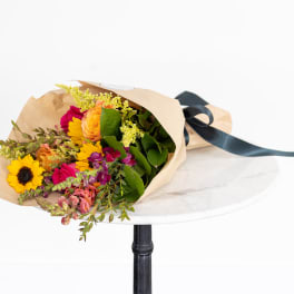 Bouquet of sunflowers, roses, and mixed blooms wrapped in tan paper