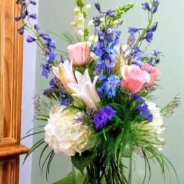Mixed bouquet in a clear glass vase with pink roses, white lilies, and blue flowers