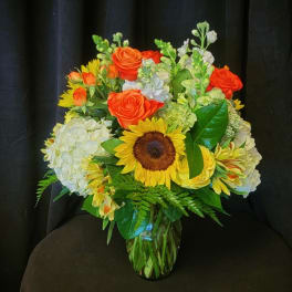 Bouquet of orange roses, sunflowers, and white hydrangeas in a glass vase