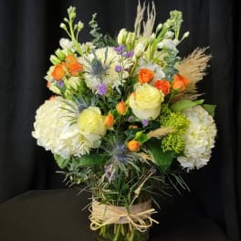 Mixed bouquet in a glass vase with white hydrangeas, roses, and orange spray roses