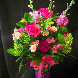 Pink and peach flower bouquet in a purple wrapped vase