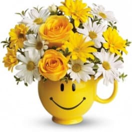 Yellow smiley-face mug holding yellow roses and white daisies