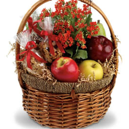 Gift basket with red flowers, apples, and wrapped snacks in a wicker basket