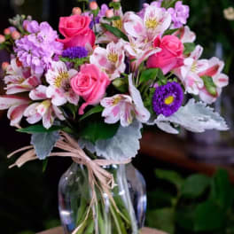 Bouquet of pink roses and purple flowers in a clear glass vase