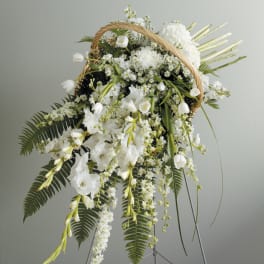 White floral standing spray on an easel with a wicker handle