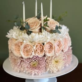 Round floral cake with pale roses, chrysanthemums, and white candles