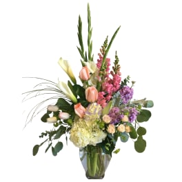 Tall mixed bouquet with peach roses, white calla lilies, and purple flowers in a glass vase