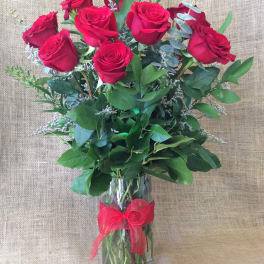 Tall arrangement of red roses in a clear glass vase with a red bow