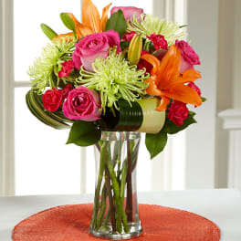 Bouquet of pink roses, orange lilies, and green spider mums in a glass vase