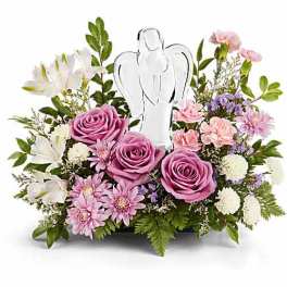 Pink roses and white flowers arranged around a clear angel figurine