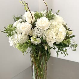 White roses and hydrangeas in a clear glass vase with greenery