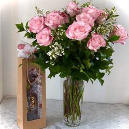 Pink roses in a clear glass vase beside a chocolate gift bag