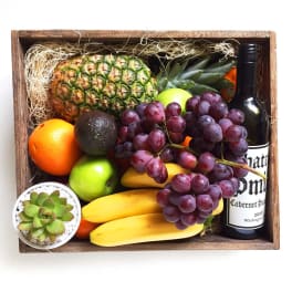Fruit gift box with grapes, pineapple, bananas, citrus, avocado, and a wine bottle