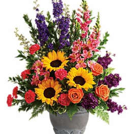 Tall mixed arrangement with sunflowers, orange roses, pink carnations and purple blooms in a gray urn