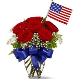 Red roses in a glass vase with an American flag and blue ribbon