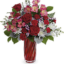 Red and pink bouquet with roses, carnations, and white mums in a tall red glass vase.