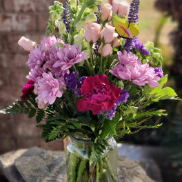 Mixed pink and purple flowers in a clear glass vase with a butterfly pick