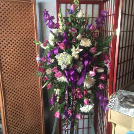 Tall standing spray of pink, purple, and white flowers with purple ribbon