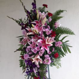 Tall standing floral spray with pink lilies and purple flowers on an easel