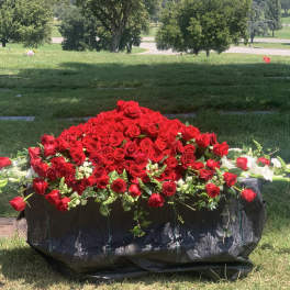 Large red rose arrangement in a black container on grass
