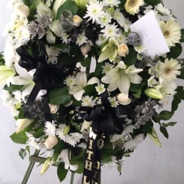 Large white floral wreath with black ribbons on a stand