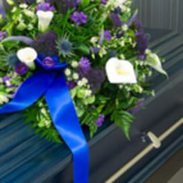 Purple and white floral spray on a casket with a blue ribbon