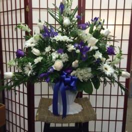 White and purple floral arrangement in a white vase with a blue ribbon