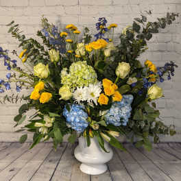 Large mixed flower arrangement in a white pedestal vase