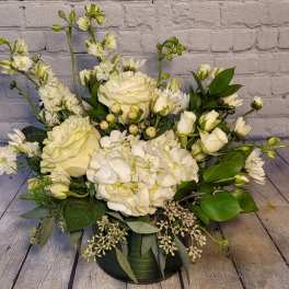 White roses and hydrangeas in a low green vase with mixed greenery