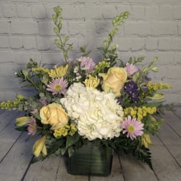 Mixed bouquet with white hydrangea, yellow roses, and pink daisies in a dark vase