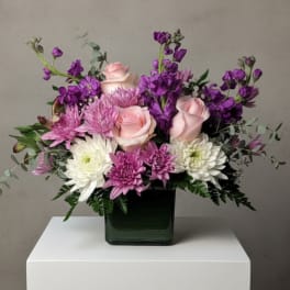 Pink roses and purple chrysanthemums arranged in a square glass vase