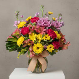 Mixed bouquet of pink, yellow, and purple flowers in a glass vase with a ribbon