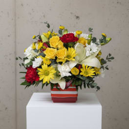 Mixed bouquet of yellow, red, and white flowers in a striped square vase
