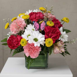 Mixed bouquet of pink, red, white, and yellow flowers in a square glass vase