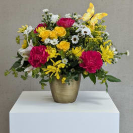 Bright mixed flower arrangement in a gold vase with a yellow butterfly accent.