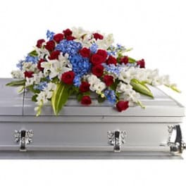 Red roses, white lilies, and blue flowers arranged on a gray casket