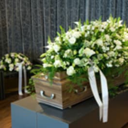 White floral casket spray on a wooden coffin with white ribbons