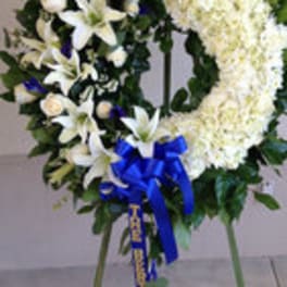 Standing funeral wreath with white lilies, white chrysanthemums, and a blue ribbon