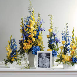 Blue and yellow floral arrangements in white containers around a framed photo