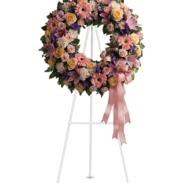 Pastel floral wreath on a white stand with pink ribbon