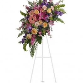 Tall floral spray with pink lilies, roses, and purple blooms on a white easel