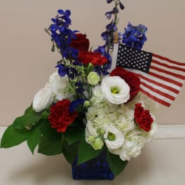 Red, white, and blue floral arrangement with an American flag in a blue vase