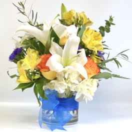 Bouquet of white lilies, yellow alstroemeria, and orange roses in a glass vase