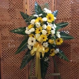 Yellow and white flower spray with a gold ribbon on a stand