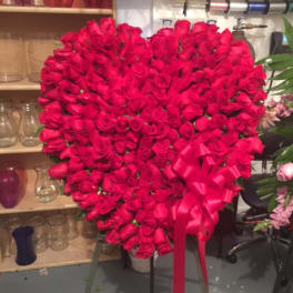 Heart-shaped arrangement of red roses with a pink ribbon bow