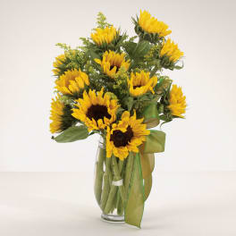 Sunflower bouquet in a clear glass vase with a green ribbon