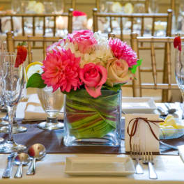 Pink floral centerpiece in a square glass vase on a set dining table