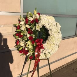 Large funeral wreath of white and red flowers on an easel with a red ribbon