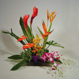 Tropical flower arrangement with orange heliconia and pink orchids in a low container