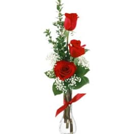 Three red roses in a clear glass vase with a red ribbon